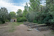 Zona de descans amb taules, bancs i una barraca de pedra seca.