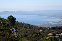 Camí que progressa a mitja vessant amb la plana empordanesa i el golf de Roses al fons (fora de ruta).