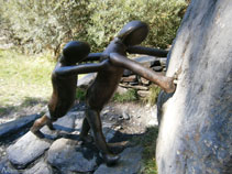 Dues persones de bronze i granit fent rodar pel pont una pedra pesada cap al riu.